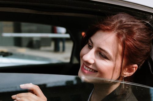 A cheerful woman smiles from the backseat of a moving taxi, city street view.